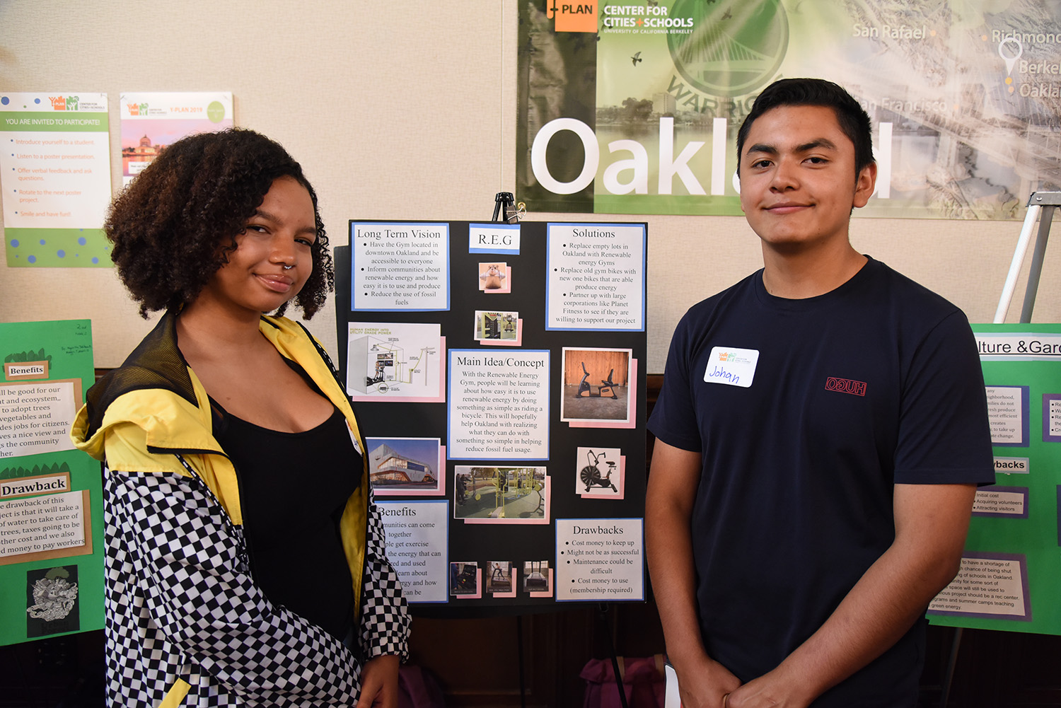 Two high school students stand in front of a presentation poster at school.